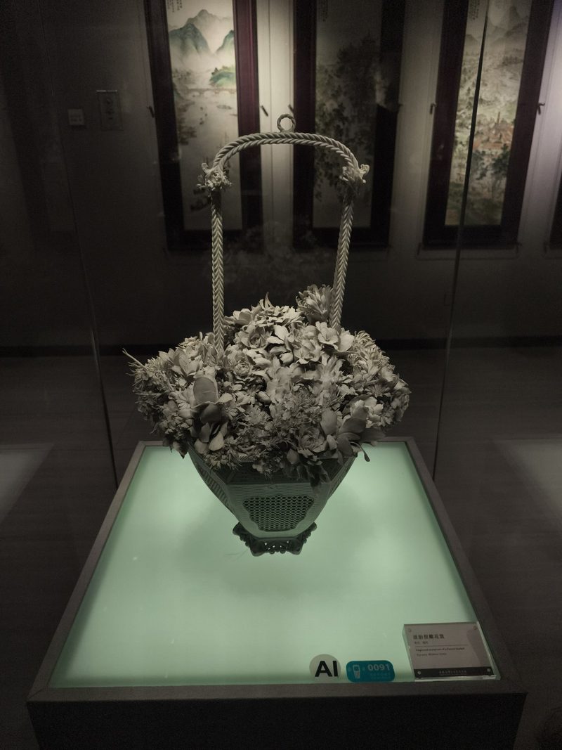 瓷塑花篮，篮中盛满白瓷花朵，底部透出青光
