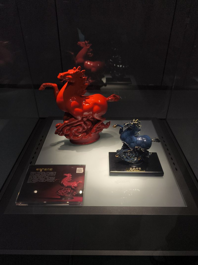 朱红色马形瓷塑立在展台上，旁边一匹为蓝色
