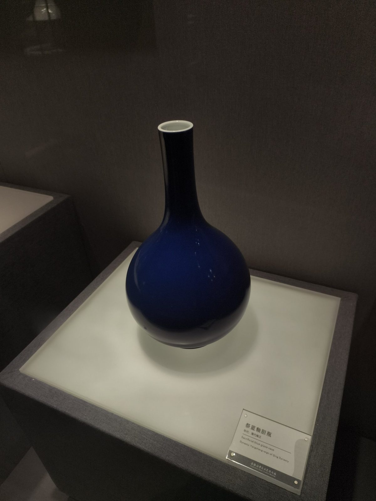 展柜里一只深蓝釉的长颈瓶，白底托着