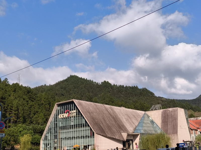 一座木质坡屋顶的现代建筑，背后是青翠山体